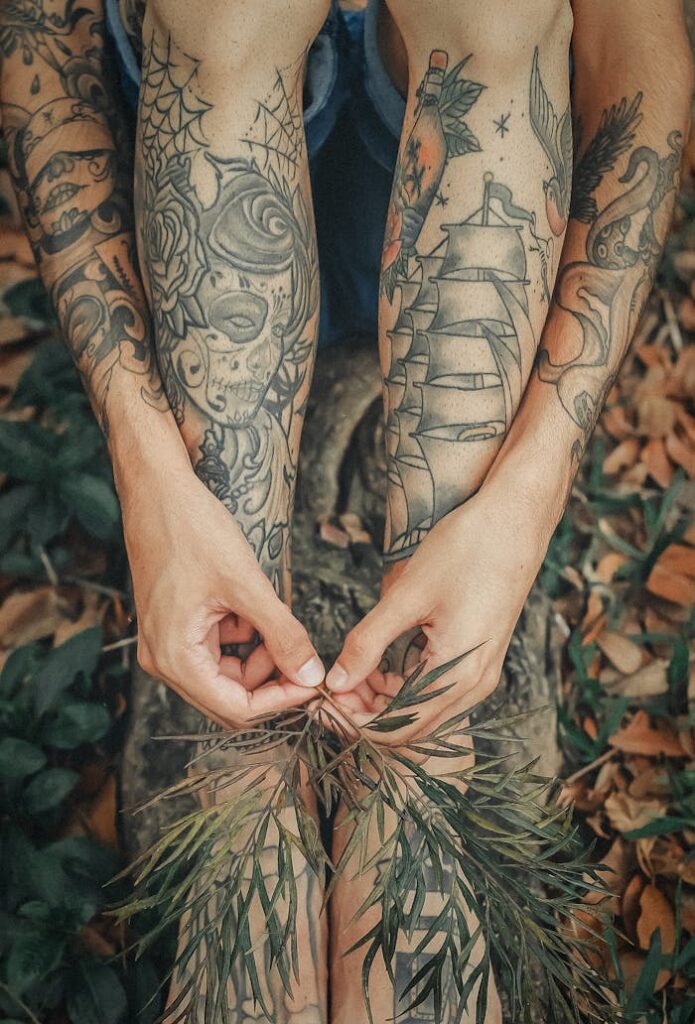 Detailed tattoos on legs and hands holding leaves outdoors, showcasing body art in nature.