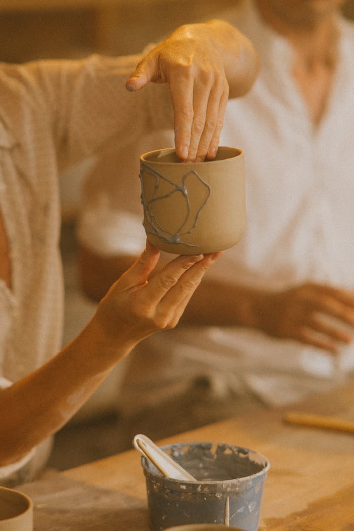 Hands working on crafting a ceramic mug in a warm-lit pottery workshop.